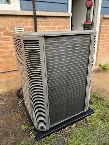 Air conditioner unit outside a building, with a cordless drill on top.