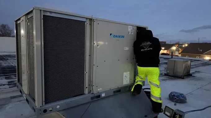A person in safety gear working on a rooftop Daikin HVAC unit.