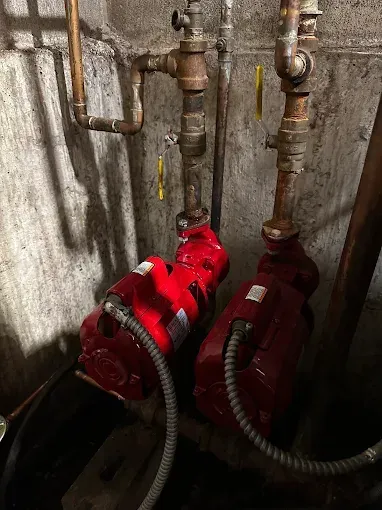 Two red water pumps connected to copper pipes in a basement setting.