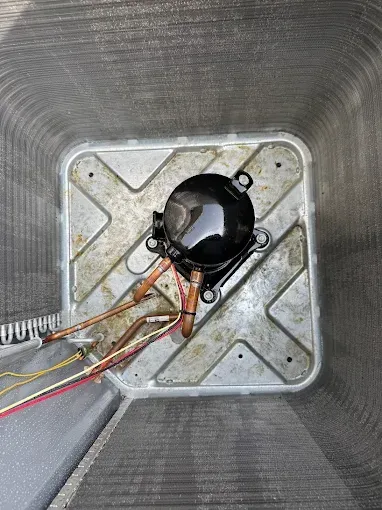 Air conditioning compressor inside its unit. Copper pipes and electrical wires visible.