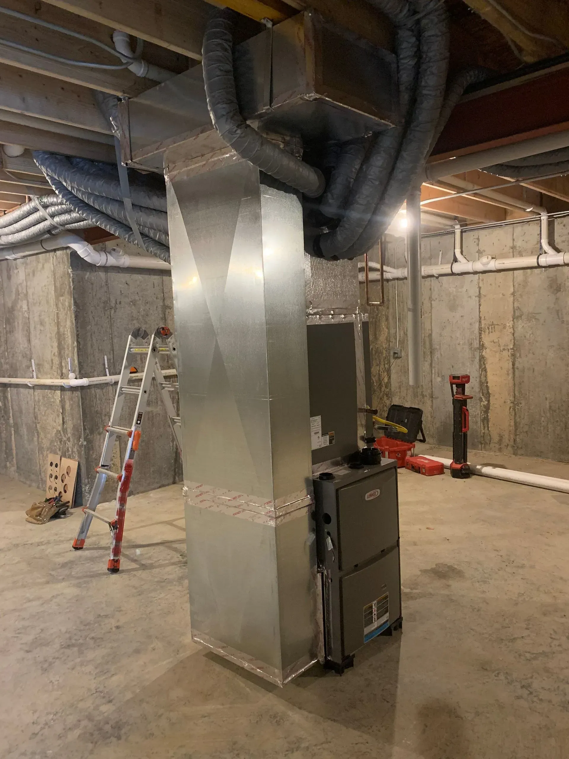 Furnace and ductwork installation in a basement with concrete walls.