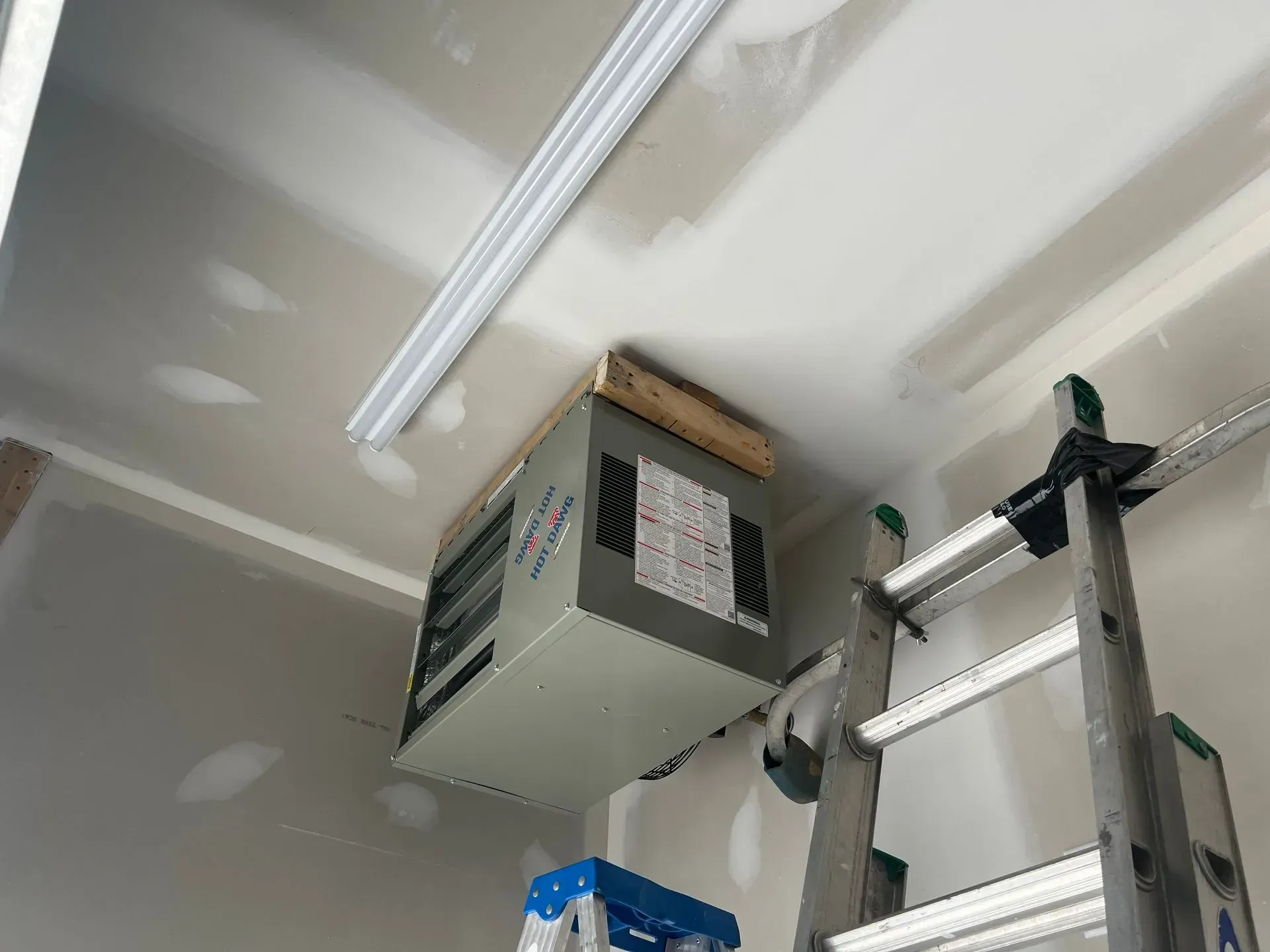 Garage ceiling with a mounted heater and ladder. Drywall and fluorescent lights visible.