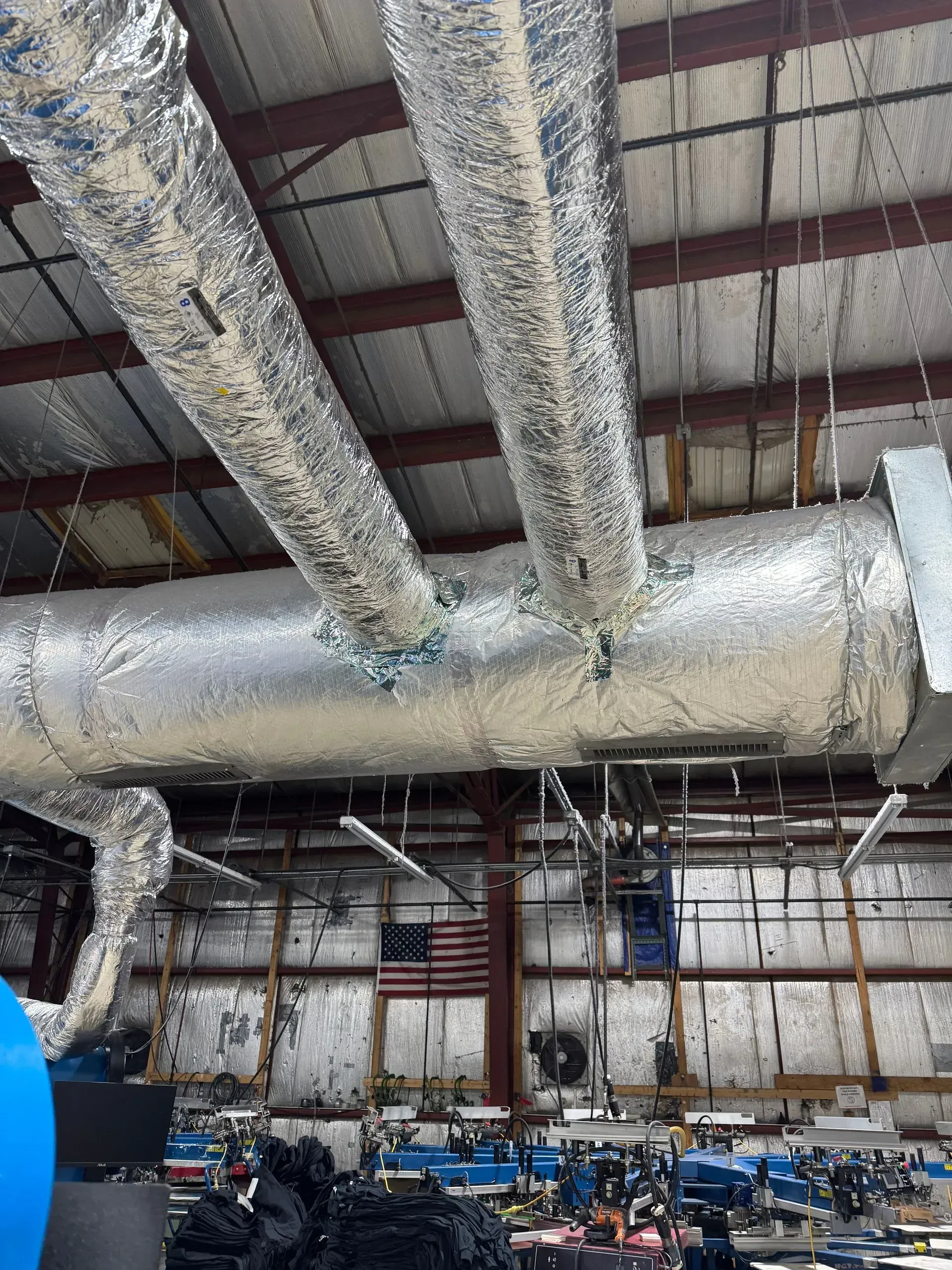HVAC ductwork wrapped in foil insulation in a warehouse with an American flag.