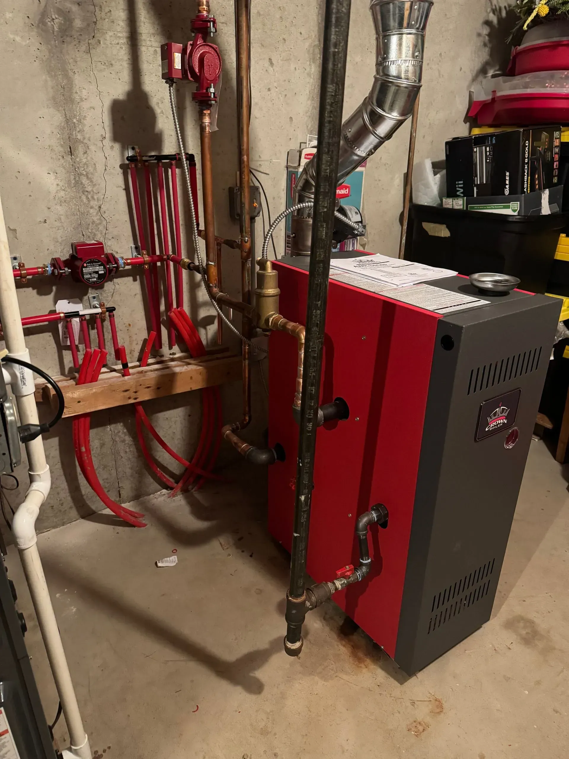 Red and gray furnace in a basement, with pipes and chimney.