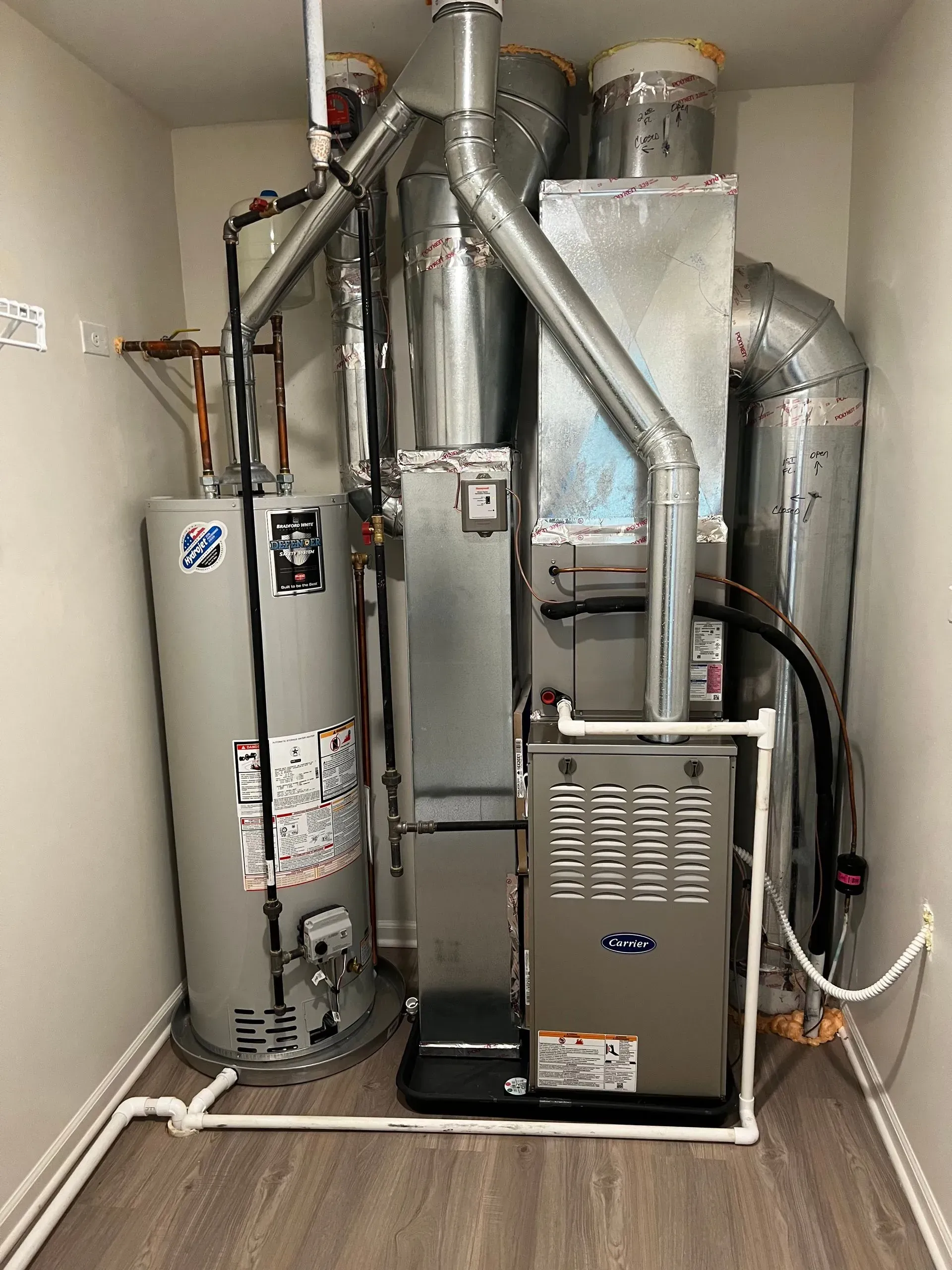 Water heater and furnace in a utility closet with ducts and pipes.