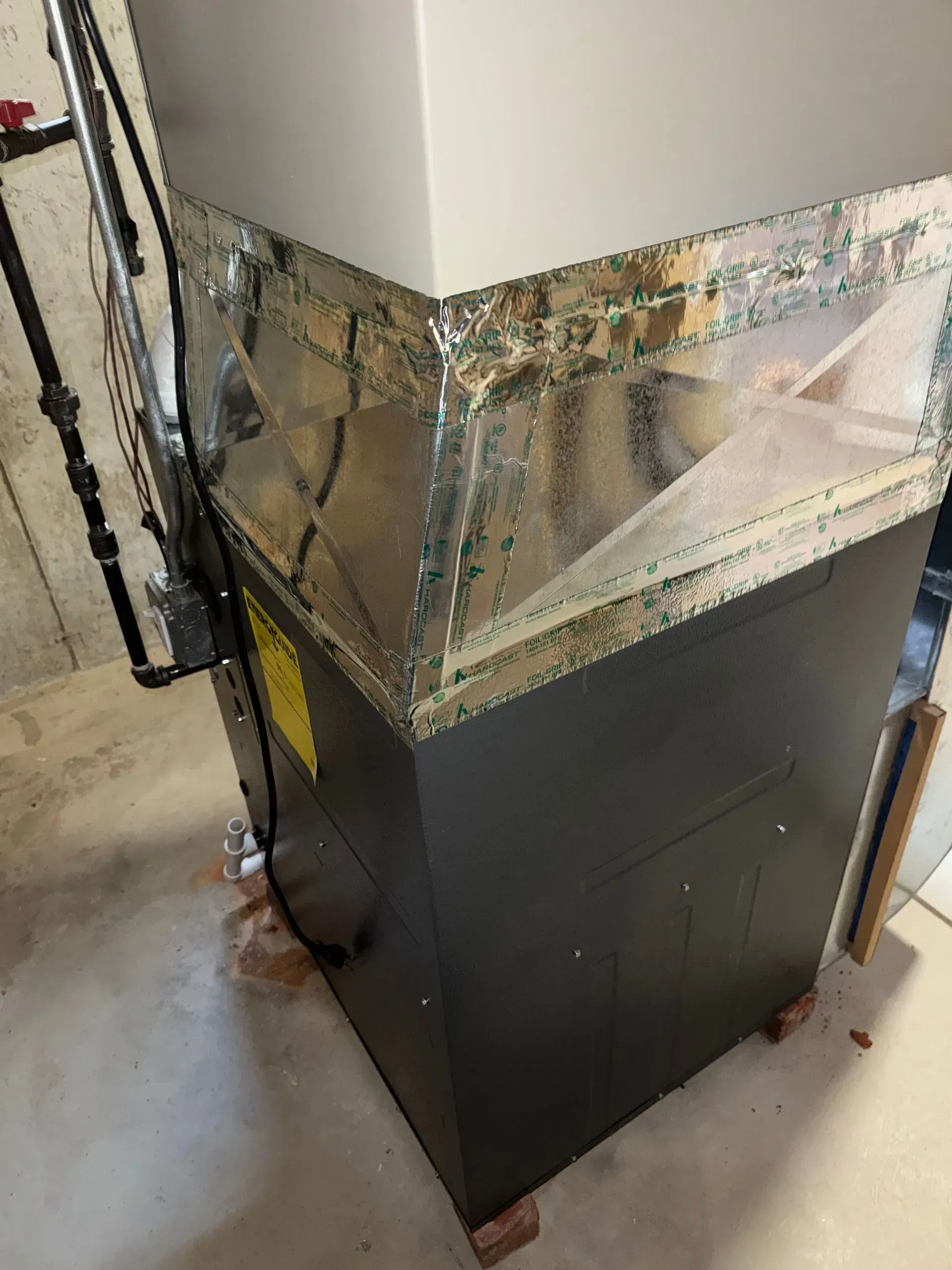 Gray HVAC unit with silver ductwork in a basement setting.