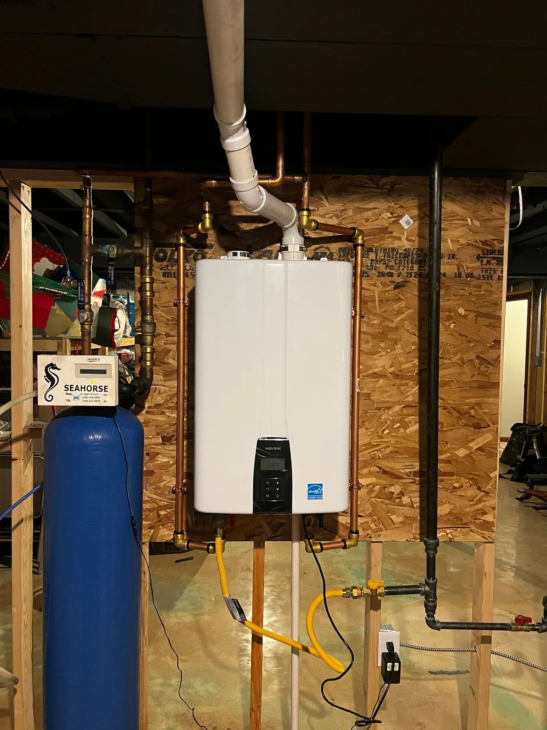 Tankless water heater and plumbing against wood paneling in a basement. Copper pipes and gas lines are visible.