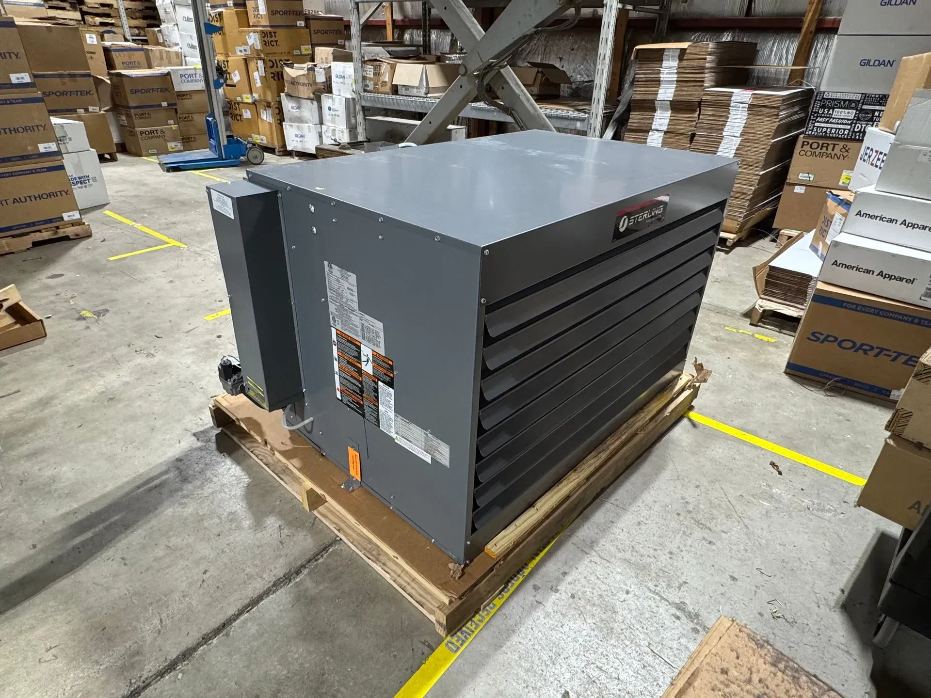 Gray industrial furnace on a pallet in a warehouse, surrounded by cardboard boxes.