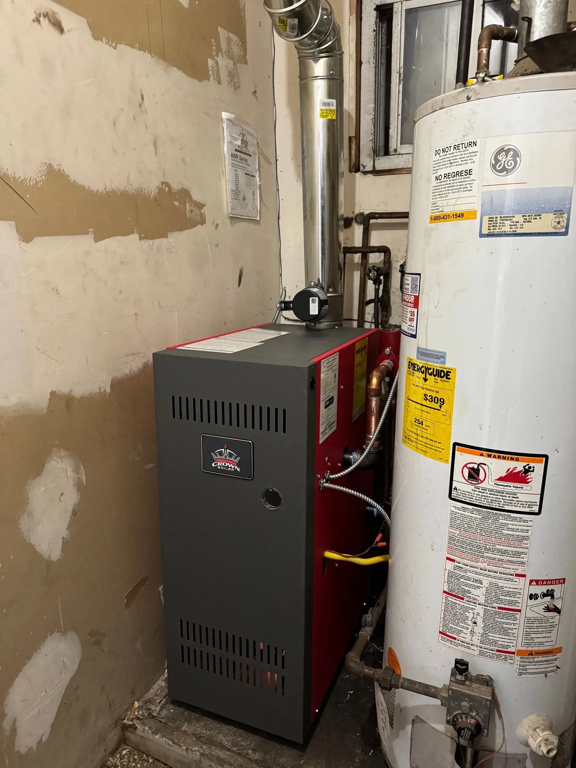 Furnace and water heater in a basement. The furnace is gray and red. A silver exhaust pipe is attached.