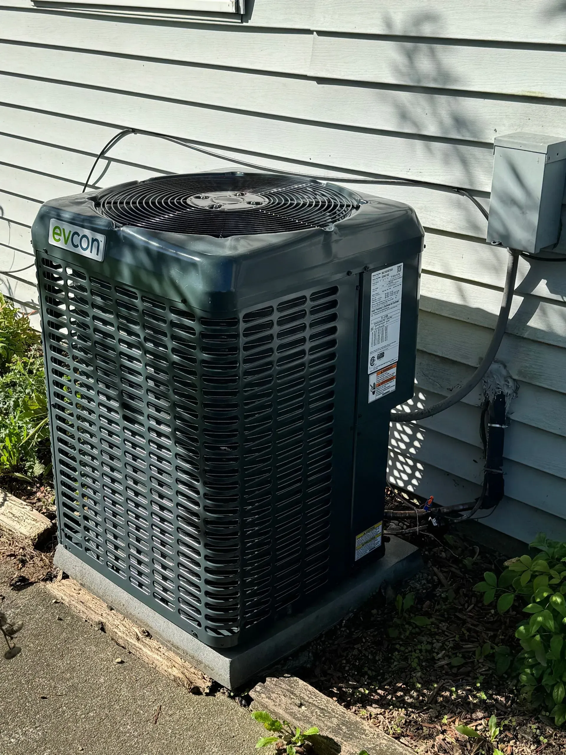 Dark green air conditioning unit outside a light gray house.