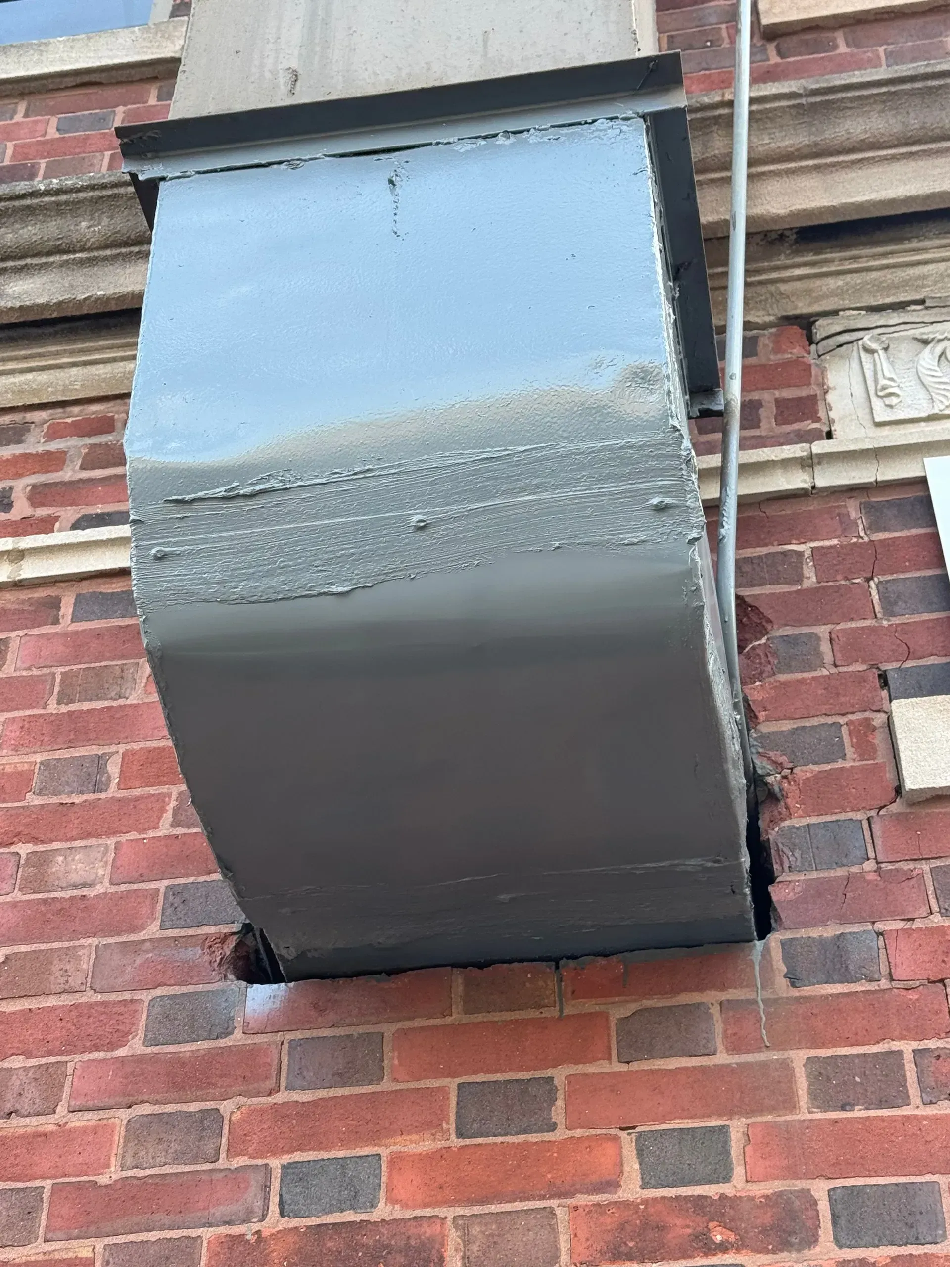 Gray metal air duct exiting a brick building, mounted to the wall.