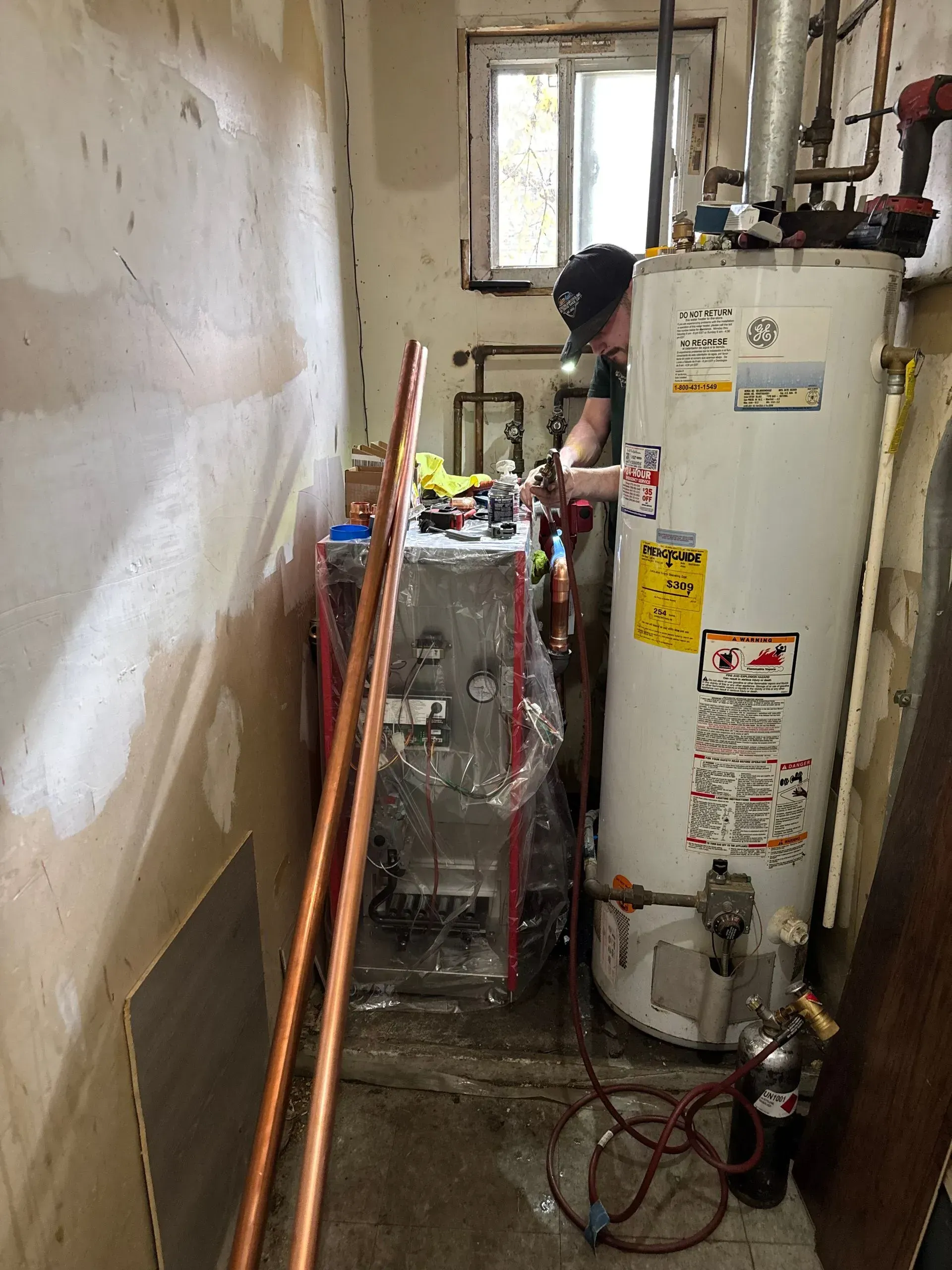 A person working on plumbing in a utility room with a water heater and copper pipes.
