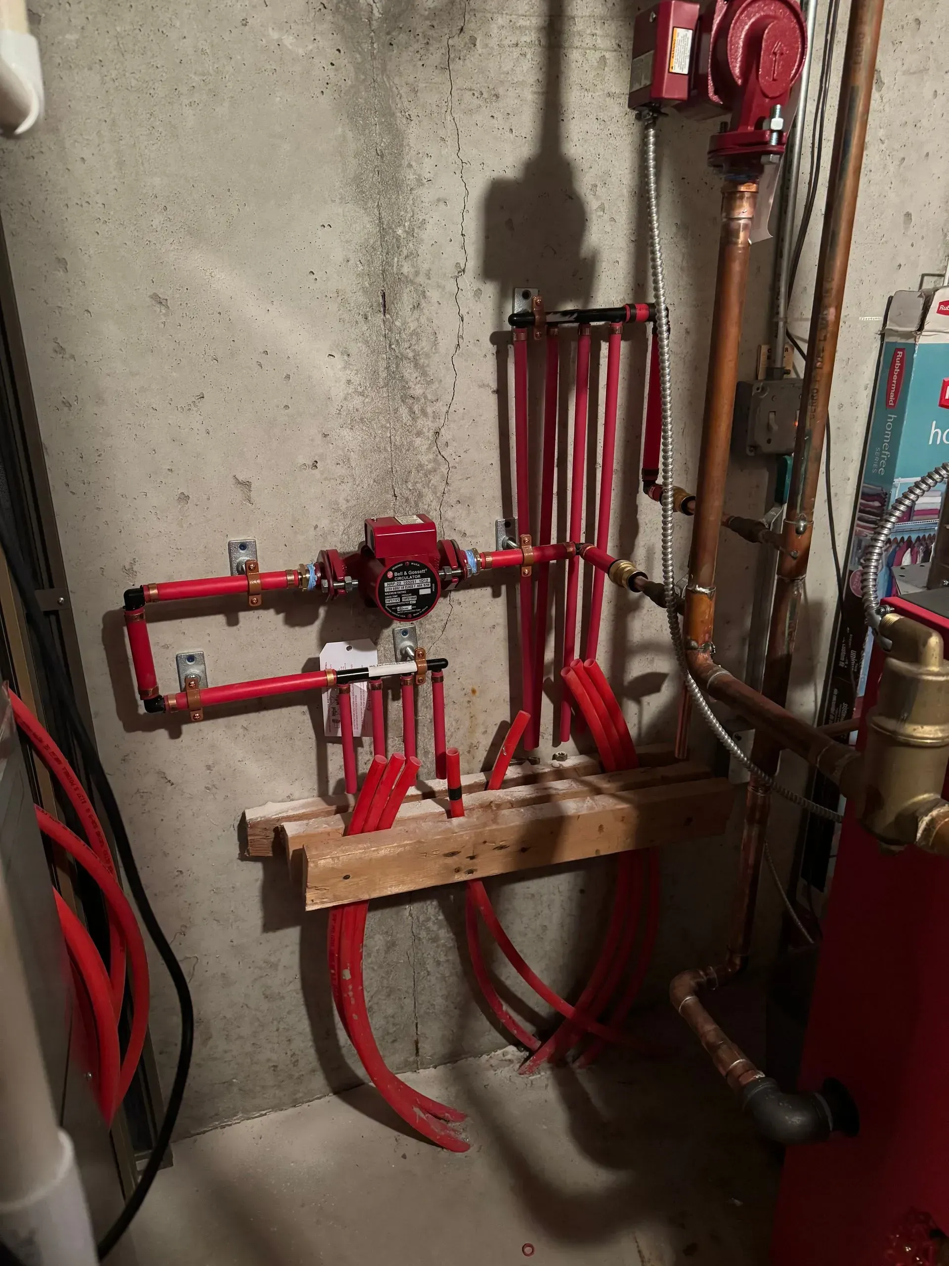Red radiant floor heating manifold system mounted on a concrete wall.