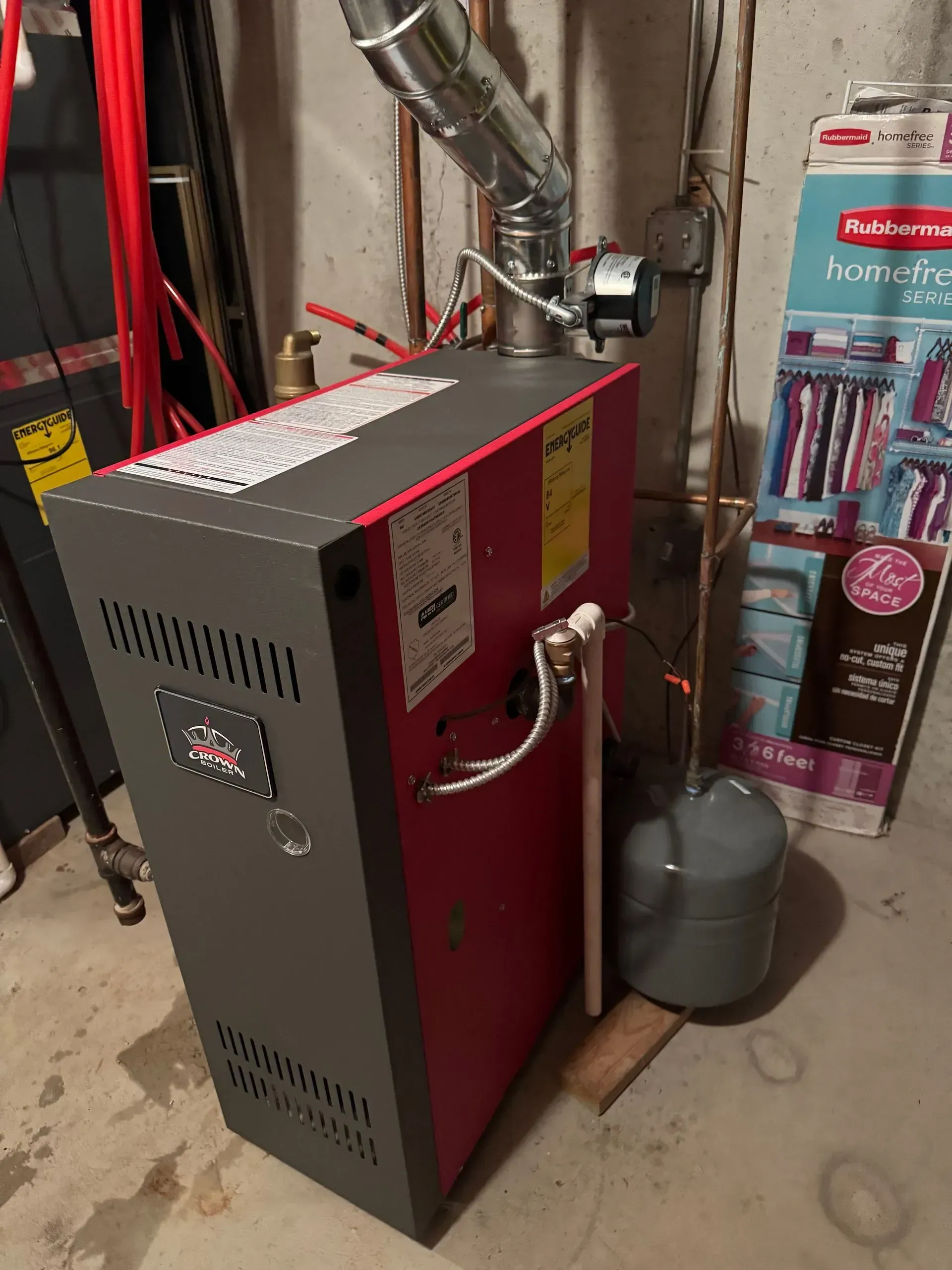 Red and gray boiler with a silver flue pipe in a basement.