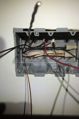 A bunch of wires are coming out of a box on a wall.