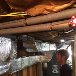 A man is standing in a basement looking at a bunch of pipes.