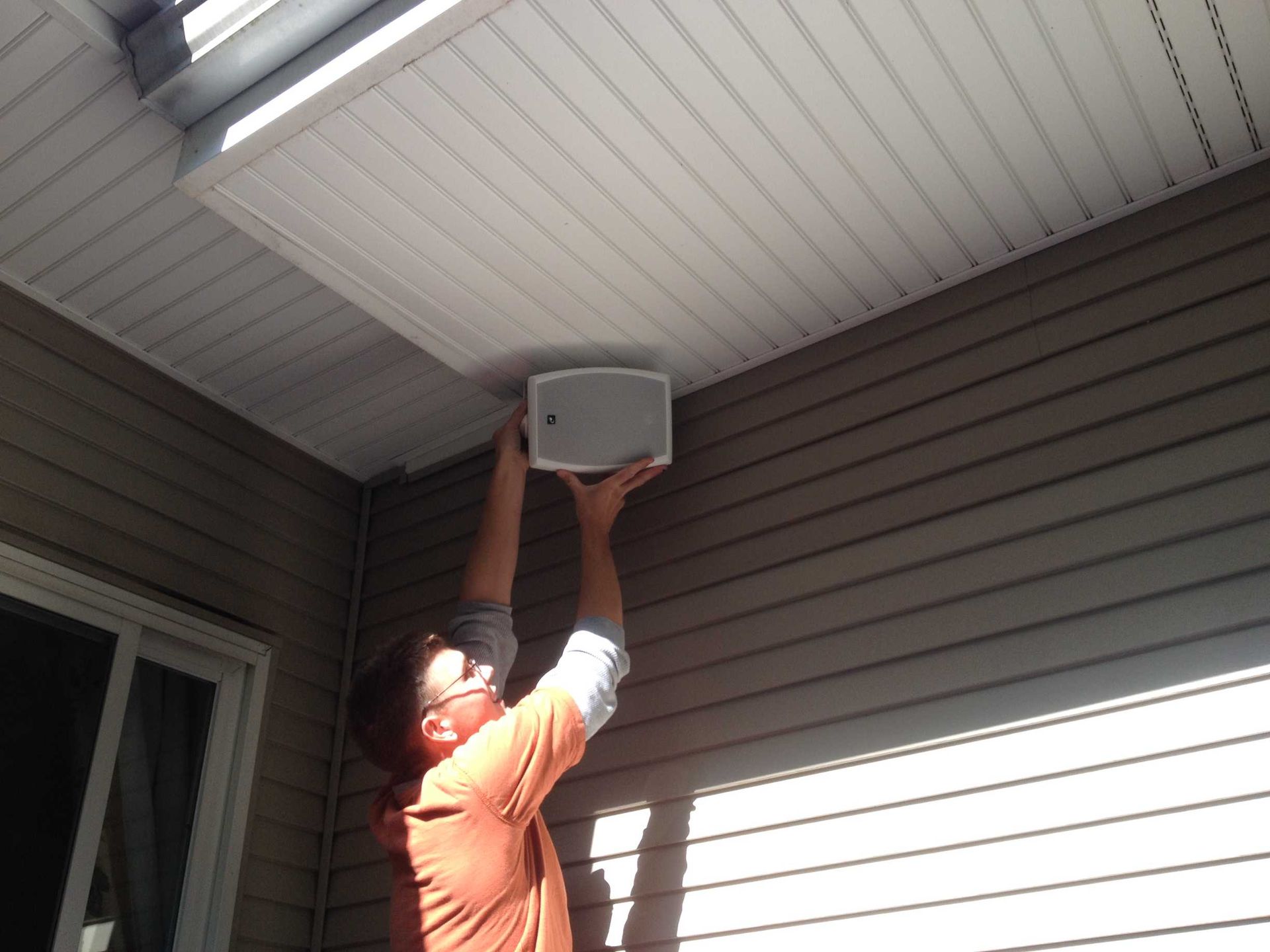A man is installing a speaker on the ceiling of a house