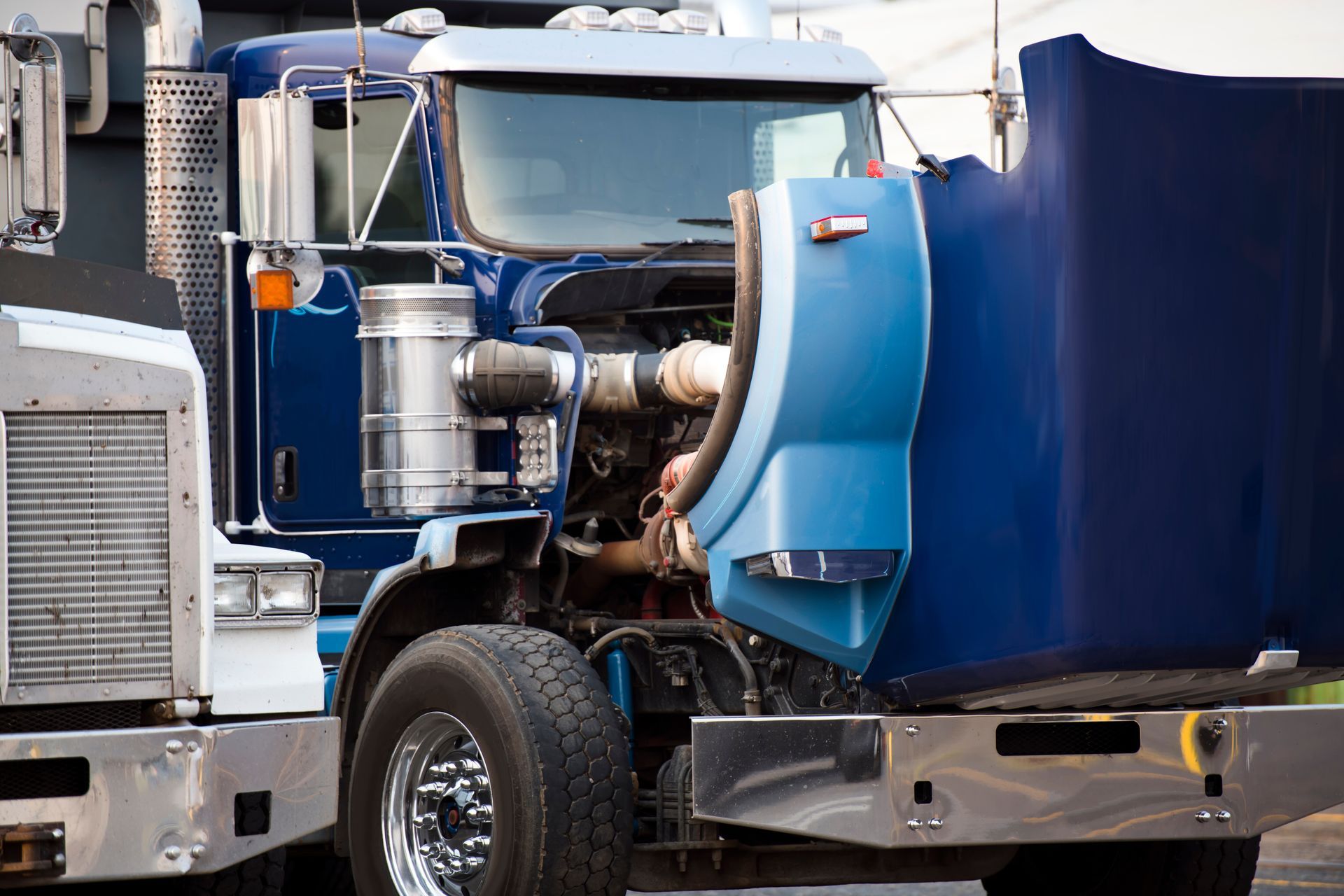 A big blue rig semi-truck with an open bonnet is standing in a parking lot for a repair service.