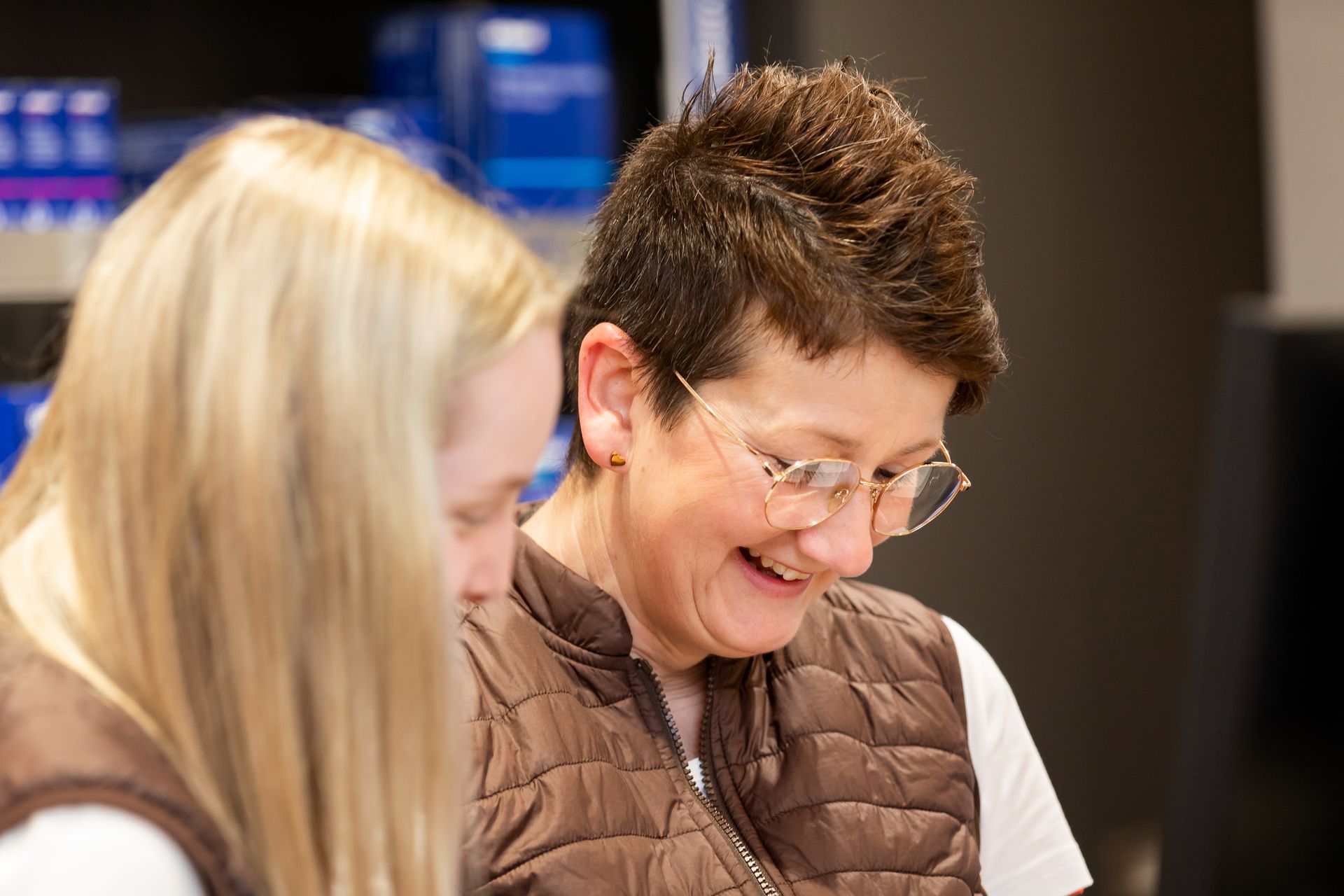 Eine Frau mit Brille steht lächelnd neben einer anderen Frau.