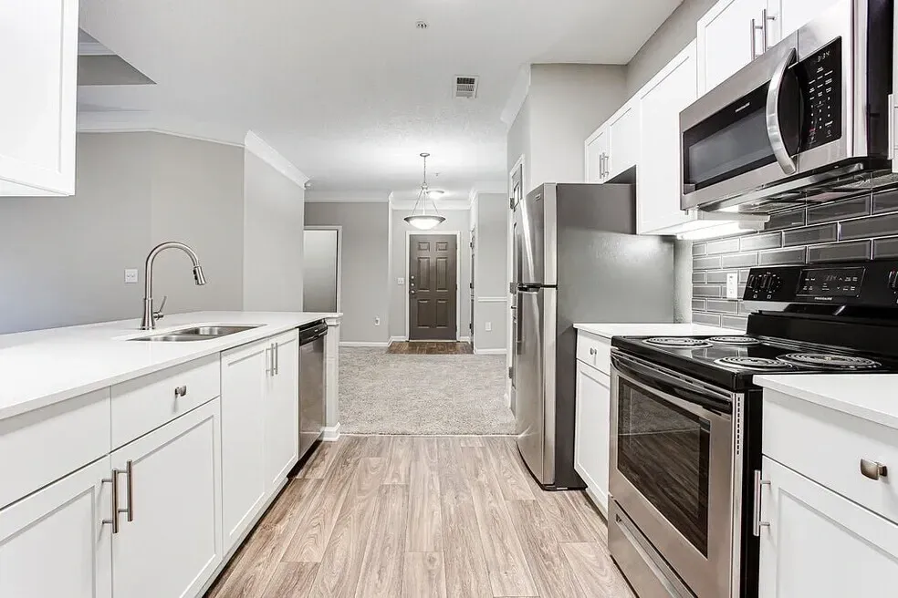 Modern white kitchen with stainless steel appliances and wood-look flooring Preserve at Mill Creek in Buford, GA