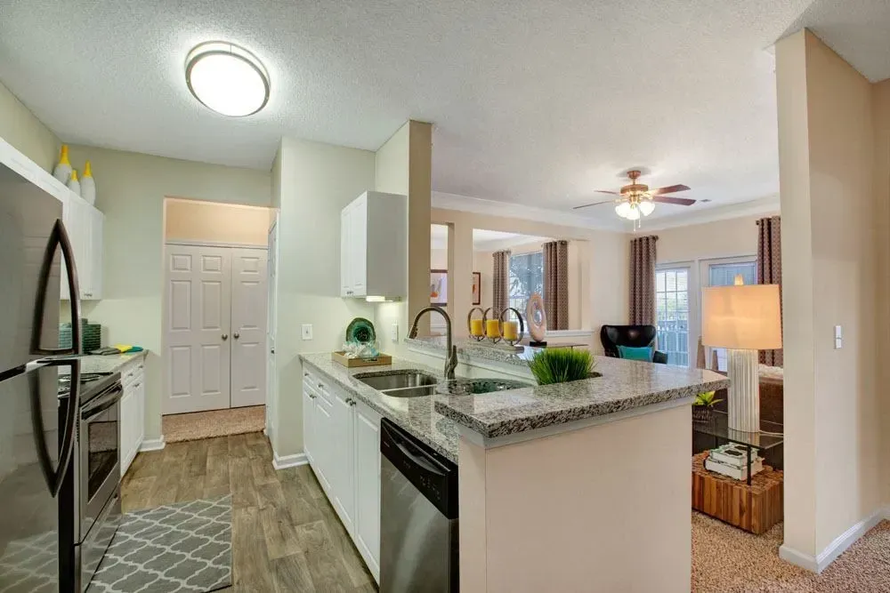Bright modern kitchen with white cabinets, granite island, and view into a sunlit living room Preserve at Mill Creek