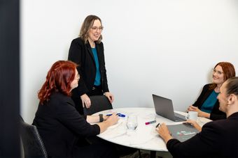 Four coworkers in a meeting around a laptop at a round table in a bright office