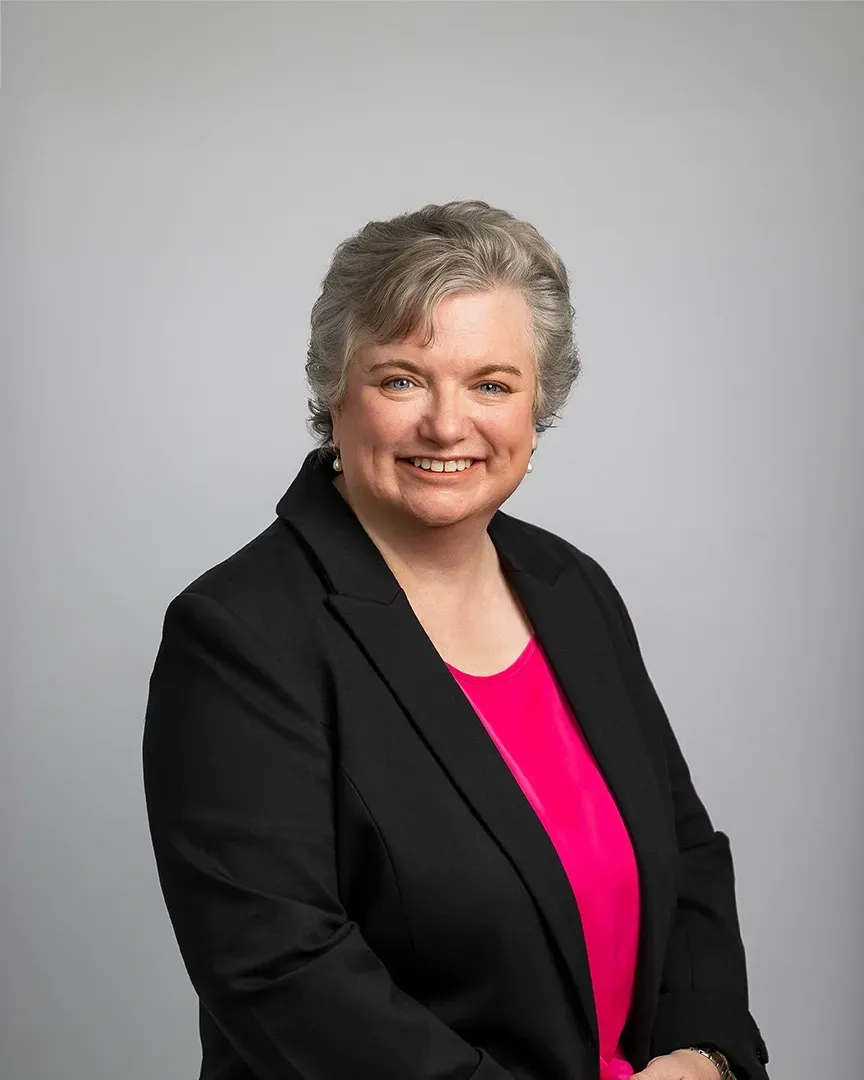 Portrait of a smiling woman in a black blazer against a light gray background