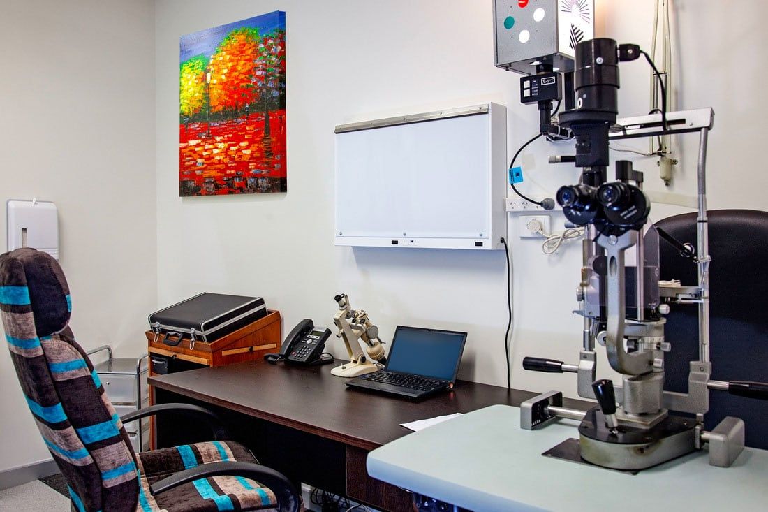 A doctor 's office with a microscope and a laptop on the desk.