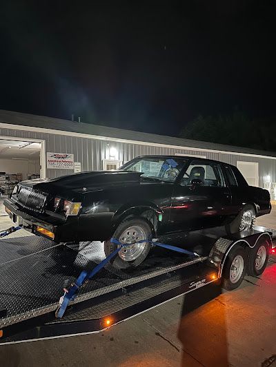 Black muscle car on a trailer in front of a building at night.