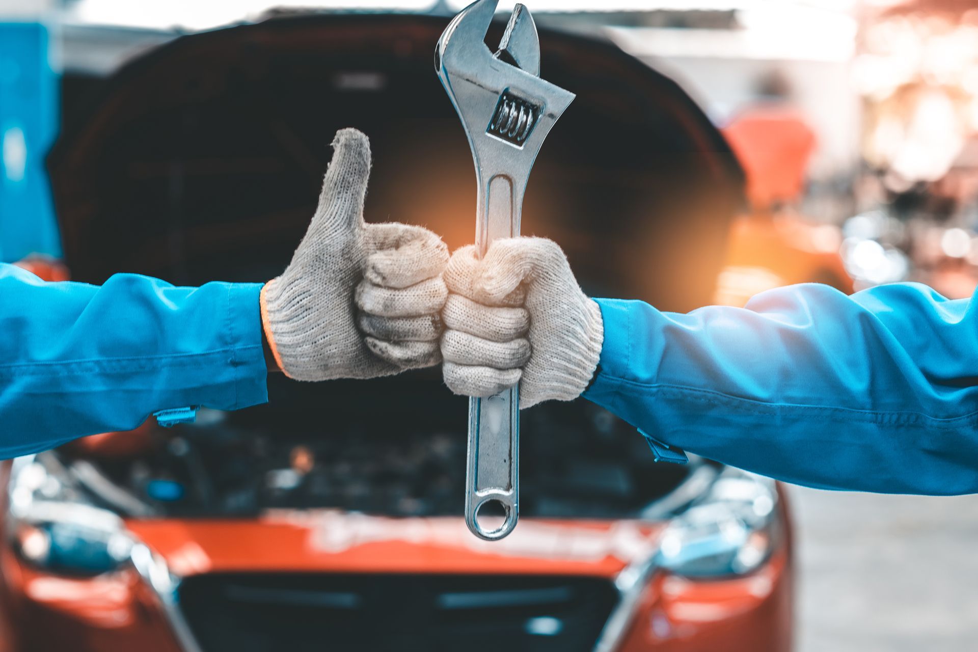 Hands holding wrench, thumbs up, in front of a car with open hood.