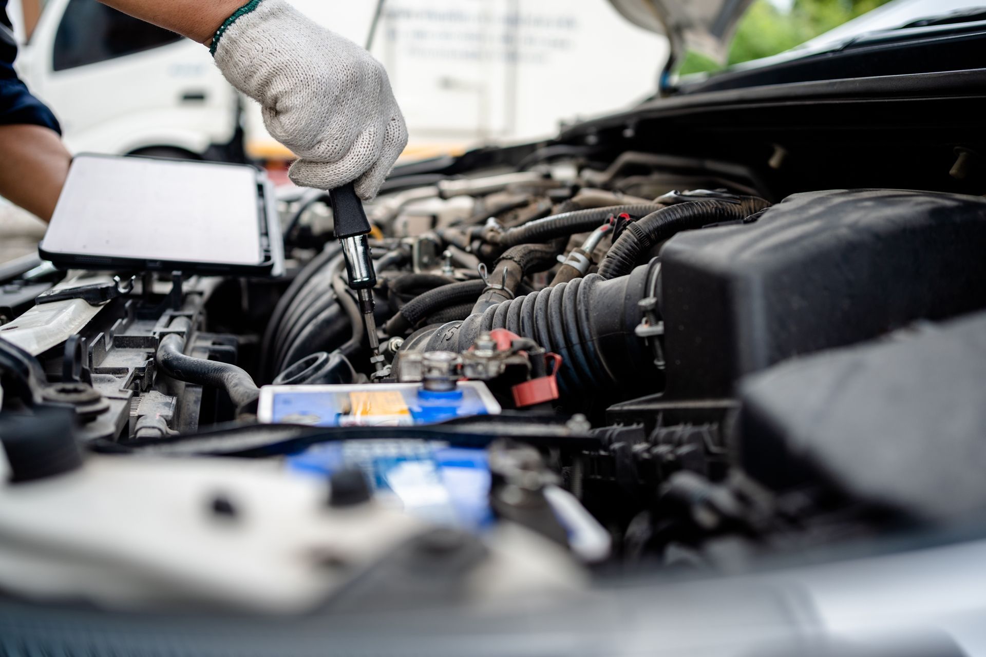 Mechanic with gloves working on car engine, using a tablet.