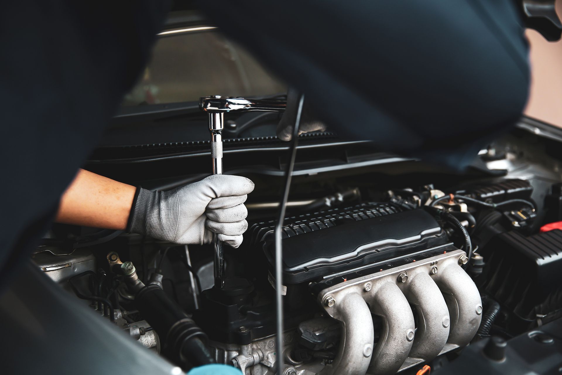 Mechanic using a wrench on a car engine, wearing gloves.