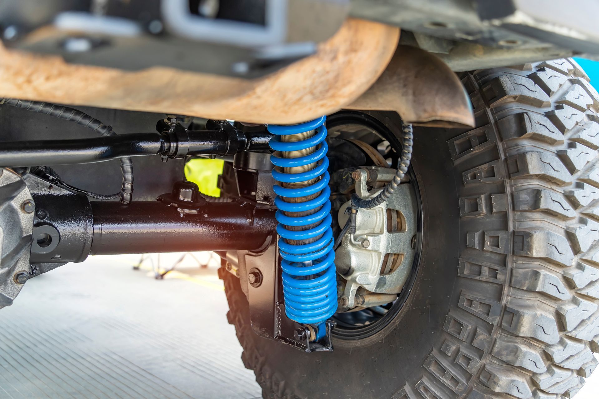 Blue shock absorber and spring on a lifted off-road vehicle with a black axle and large tire.