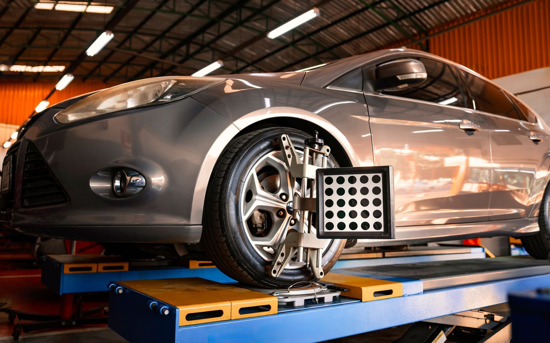 Car being aligned on a lift in a garage, a wheel attached to a calibration device.