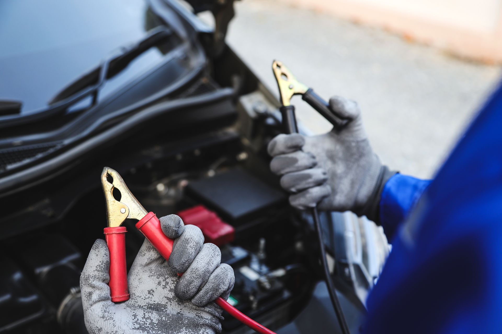 Hands holding jumper cables near a car engine.
