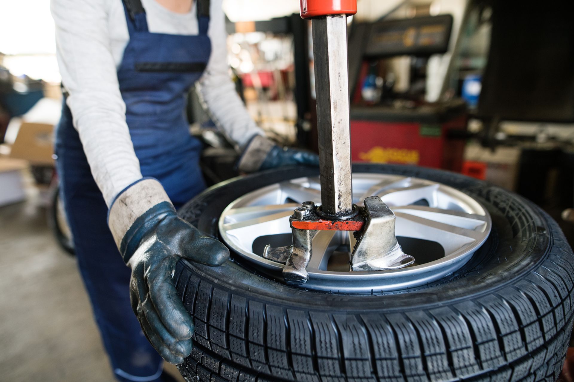 A person in work overalls uses a tire machine to change a tire in a repair shop.