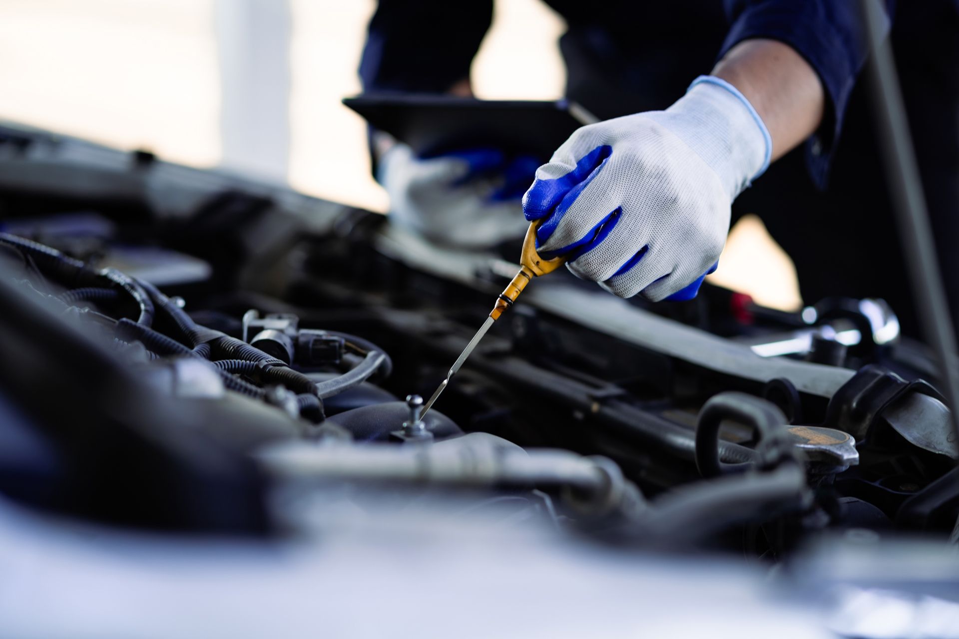 Mechanic checking oil level in car engine bay. Glove holding dipstick, dark blue uniform.