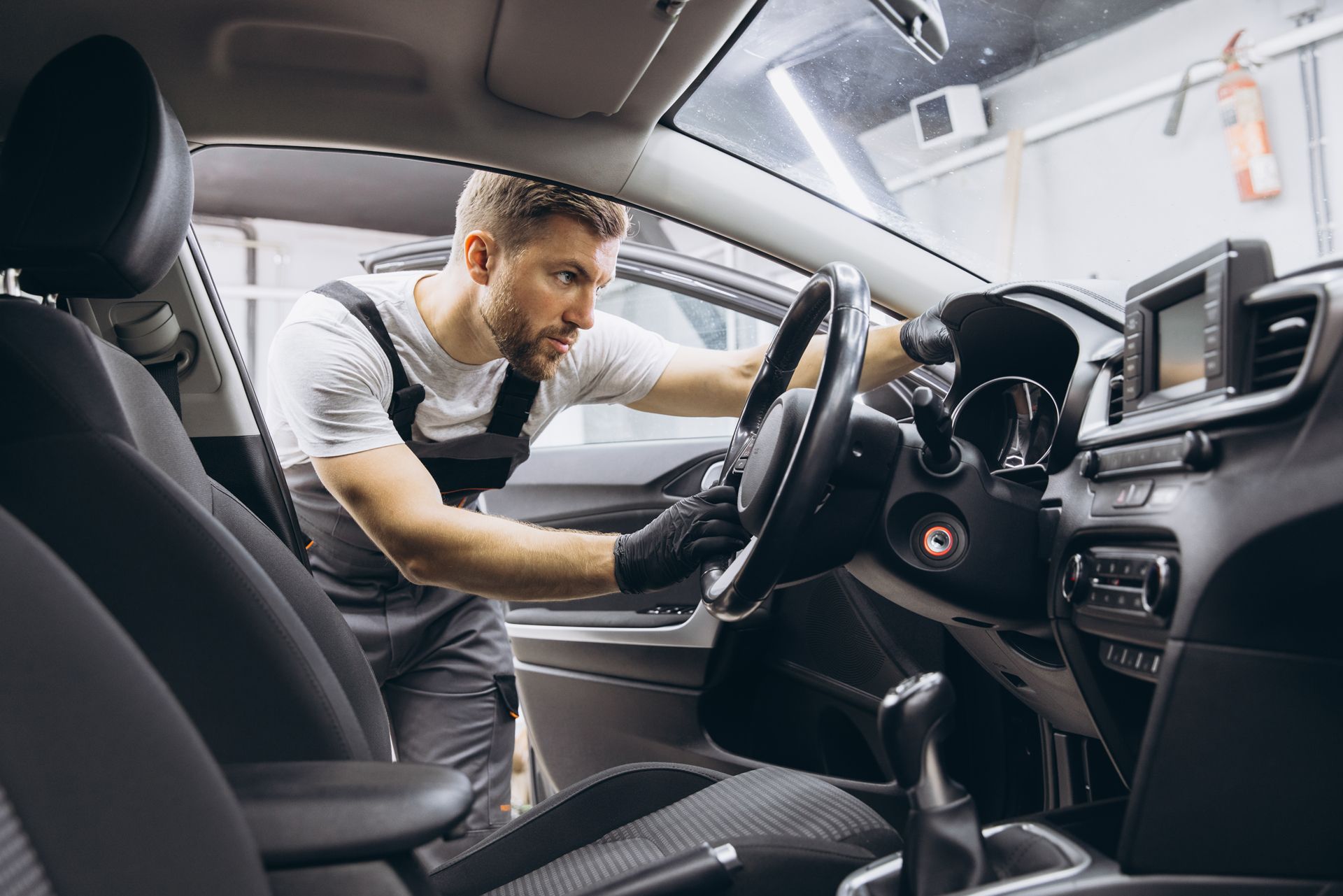 Mechanic in overalls cleans a car's interior.