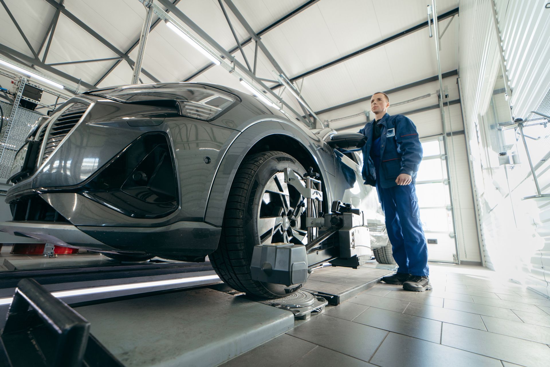 Mechanic in blue coveralls adjusts gray car wheel on a lift inside a workshop.