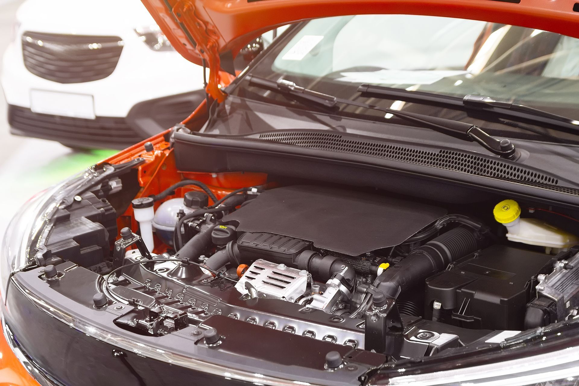 Orange car engine bay, open for inspection, with a white car in the background.