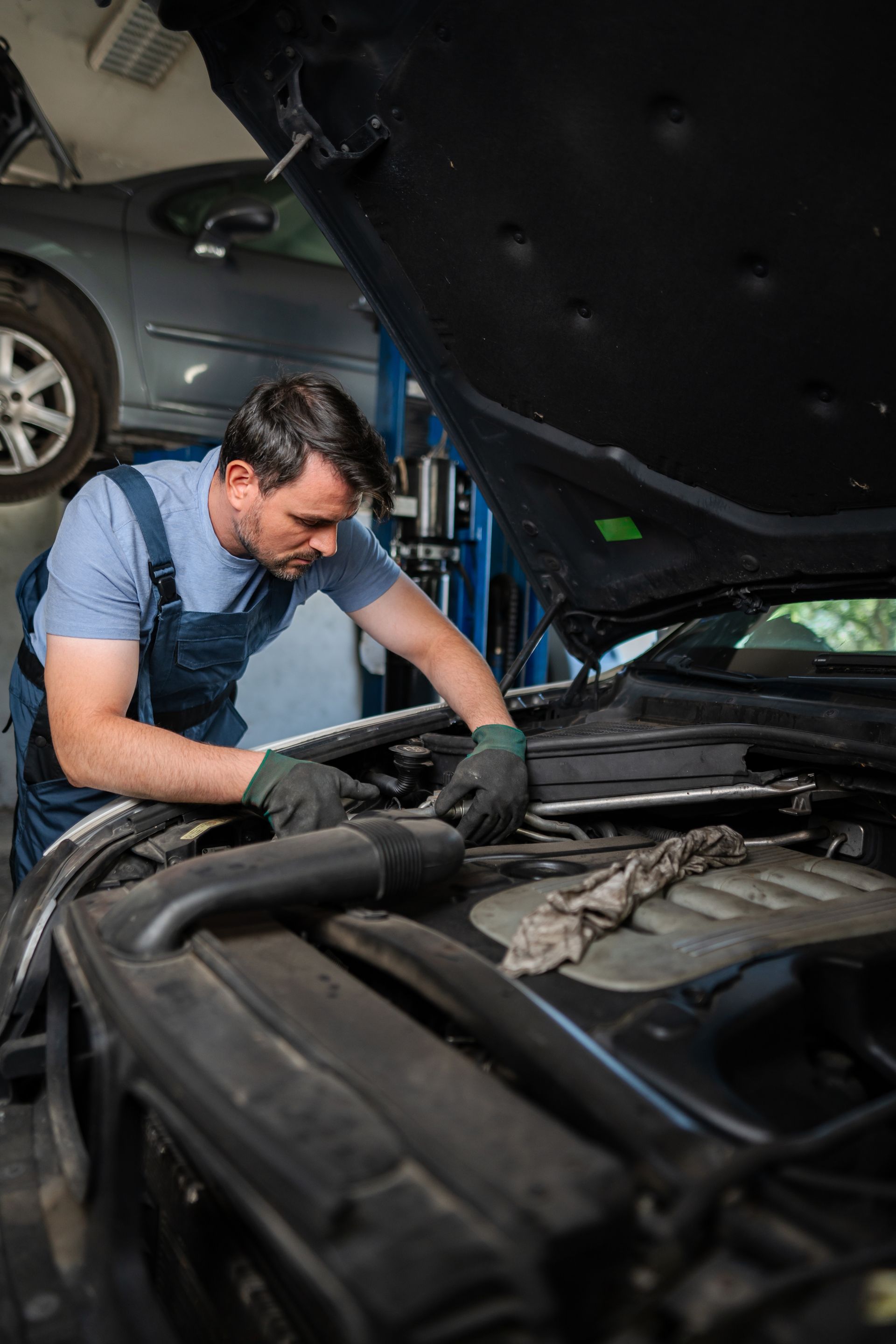 Mechanic in overalls working on a car engine in a repair shop.