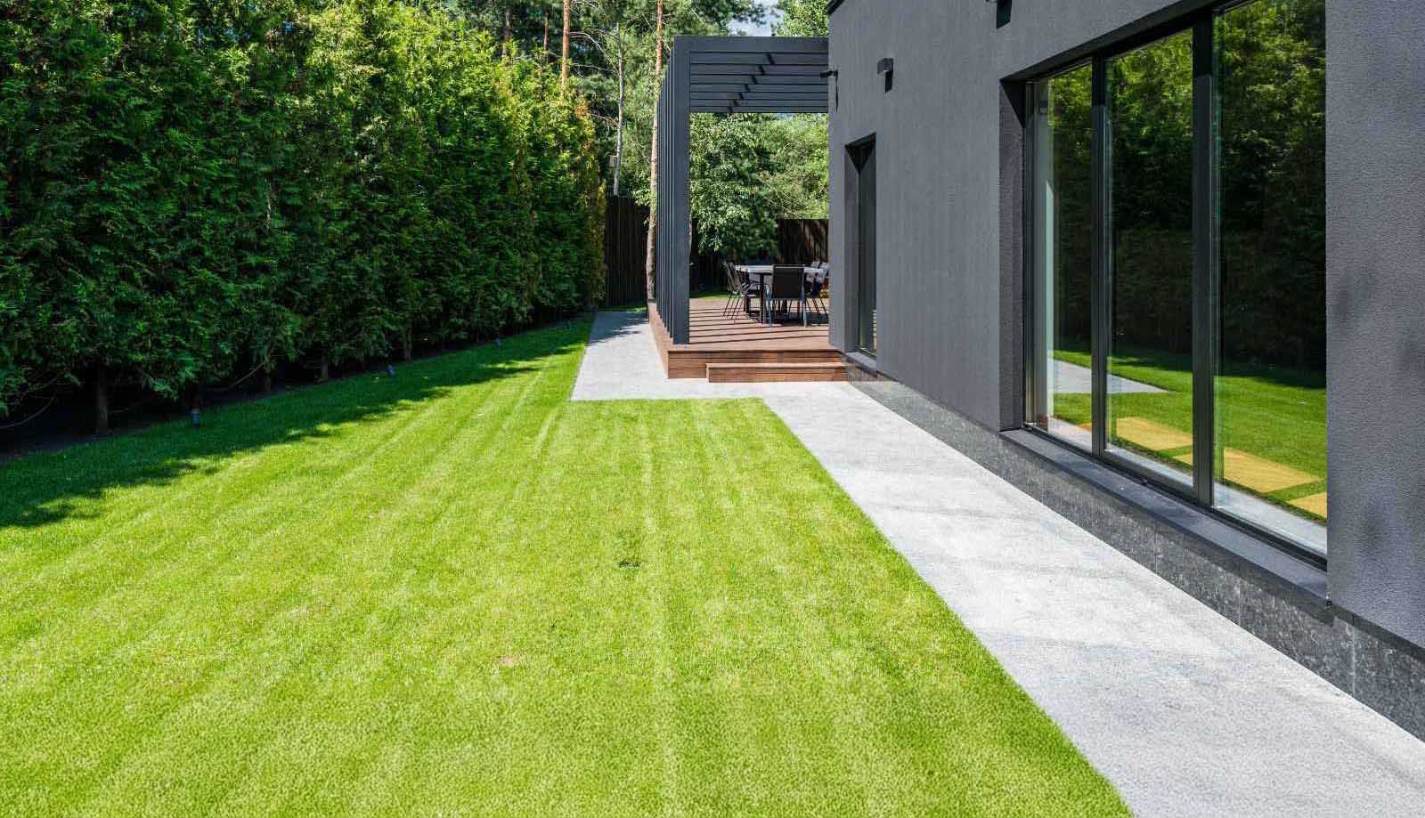 A well-maintained lawn leads to a modern house with a patio area and large windows.
