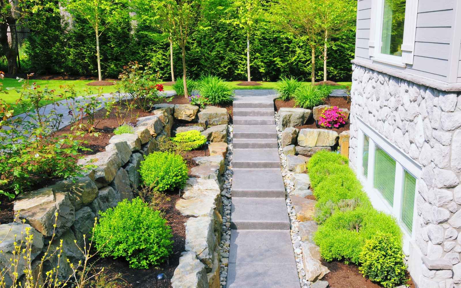 A well-maintained garden with stone walls, landscaping, and steps leads up to a house.