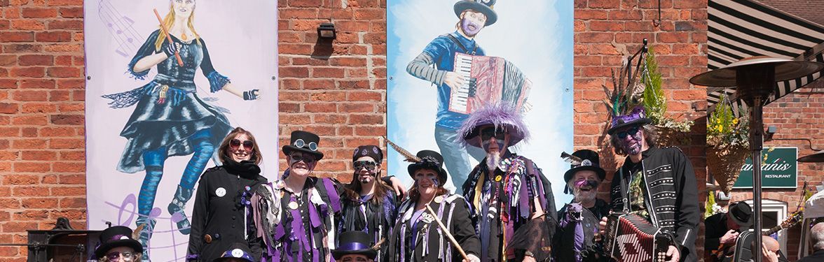 a group of people in costumes are standing in front of a brick wall with a painting on it.