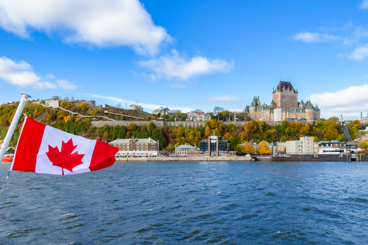 The Canadian flag waves in the foreground overlooking the St. Lawrence River and the Fairmont Le Château Frontenac.