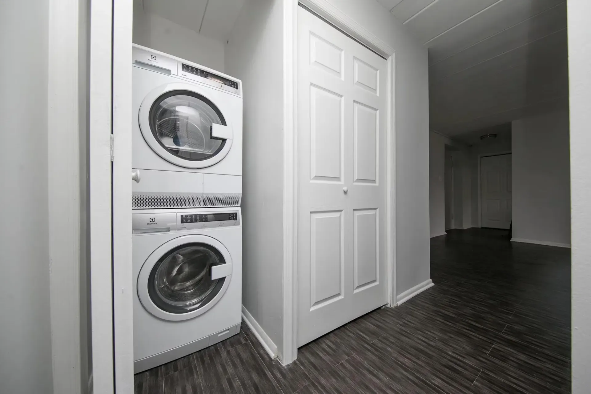 Stacked white washer and dryer in a small laundry area next to a closed white closet door and dark gray floor.