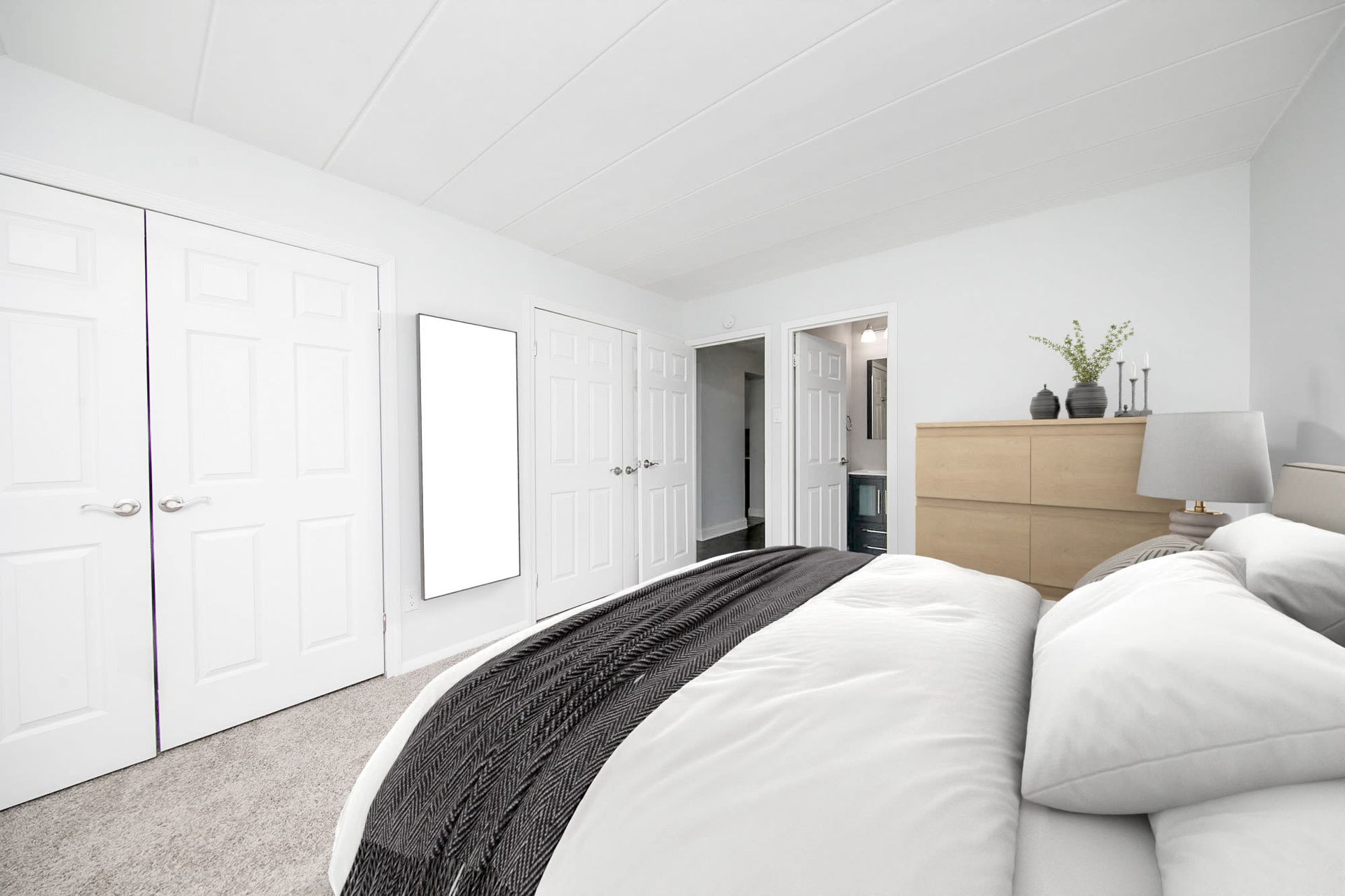 Bright bedroom with white walls, a large bed, and a light wood dresser against the wall.