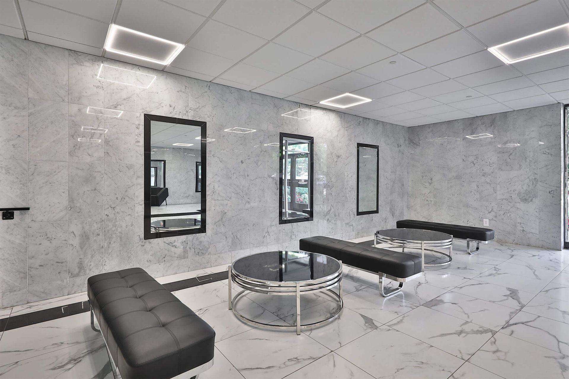 Modern marble lobby with black benches, round glass tables, and wall mirrors.