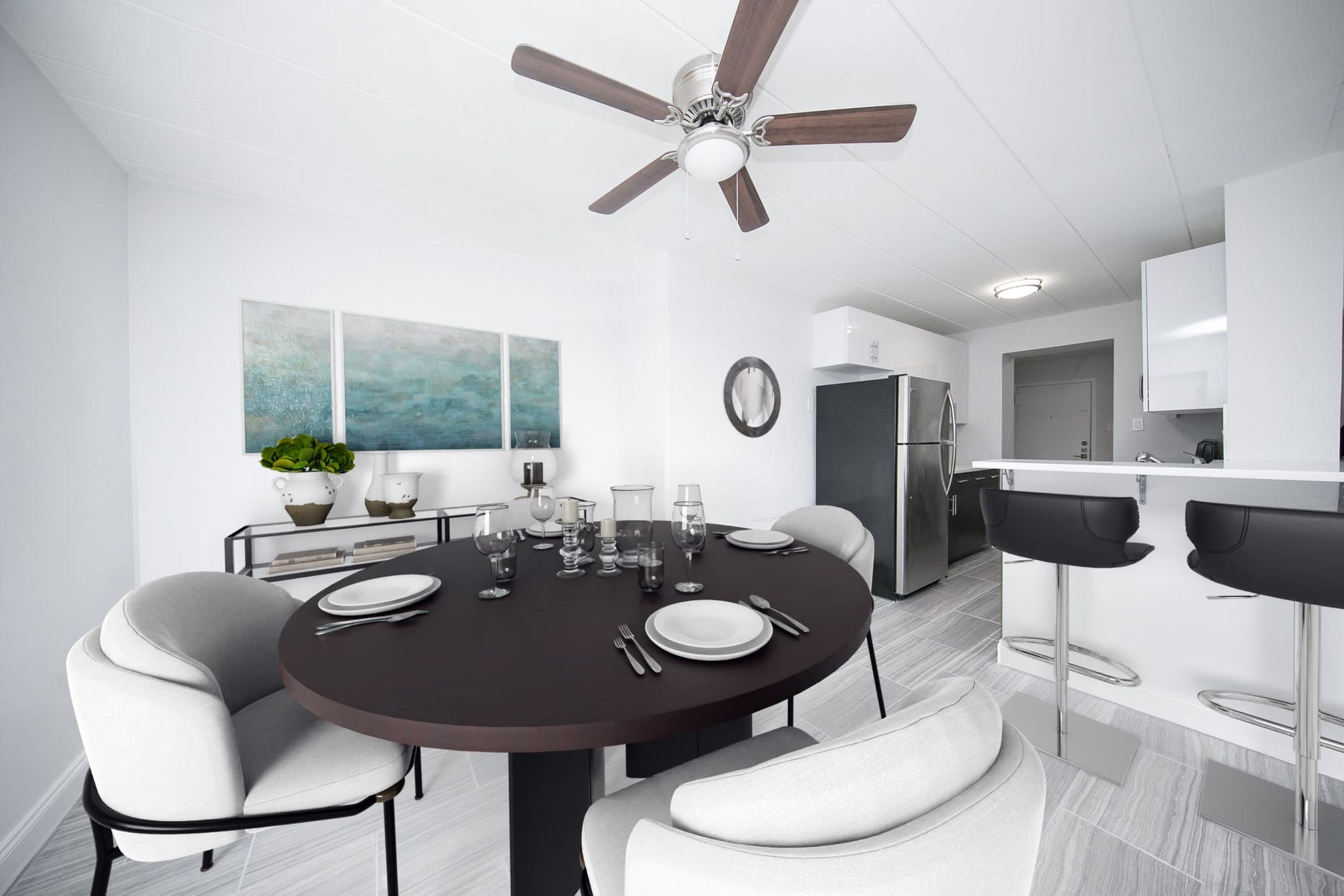 Open-plan apartment dining area with round dark table, white chairs, and a modern kitchen bar.