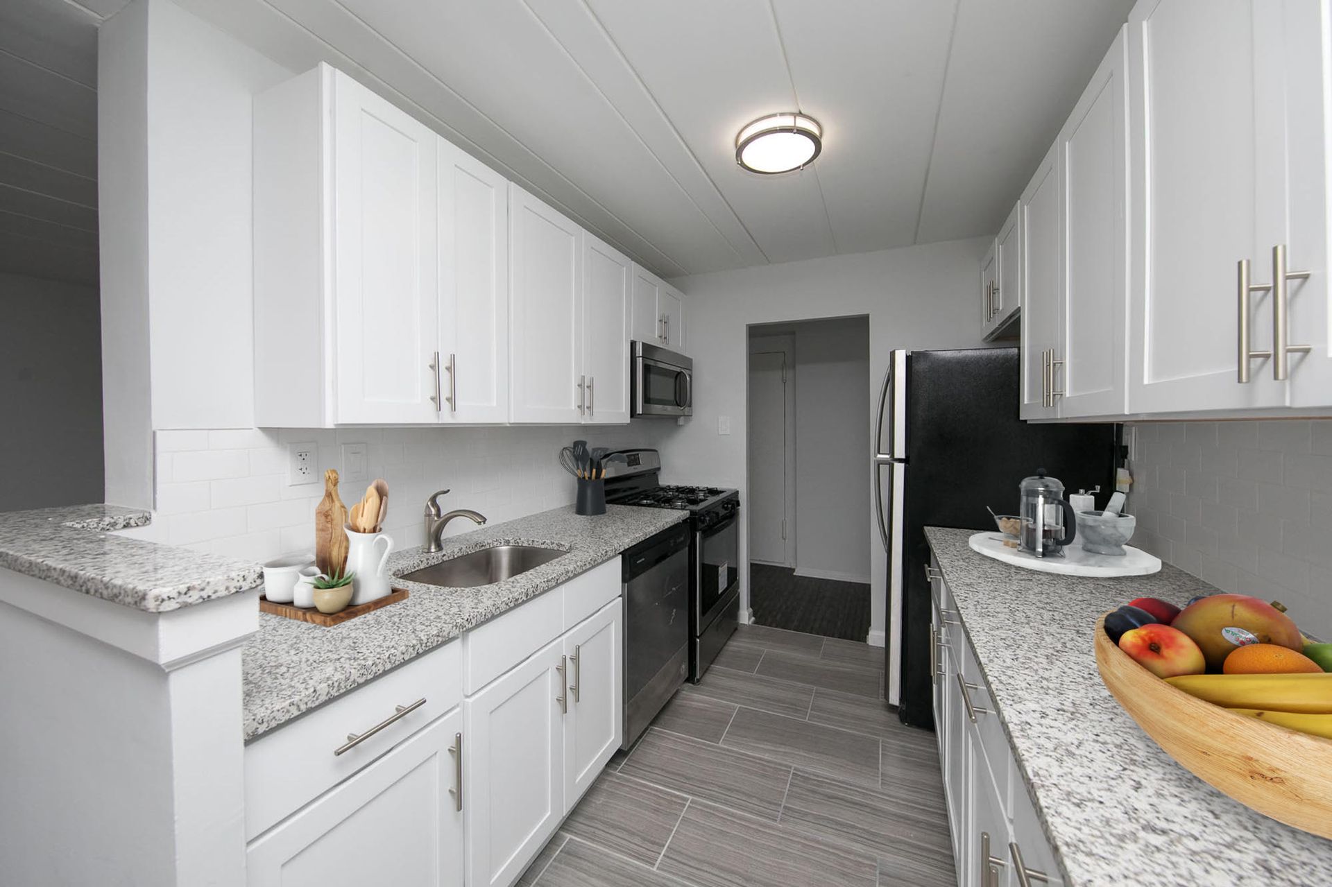 Modern white kitchen with granite countertops, stainless steel appliances, and a double sink.